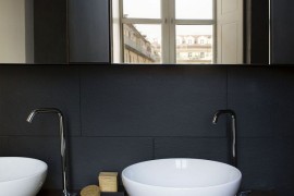 Black backdrop and white sinks along with a wooden vanity in the bathroom