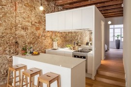 Wooden ceiling beams and stone wall stand in contrast to the sleek white kitchen
