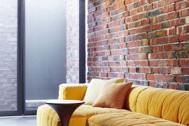 Plush couch in bright yellow adds color to the creative sitting area in brick, glass and steel