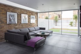 Large gray couch, brick and glass walls create a lovely contemporary living room [From: IQ Glass UK]