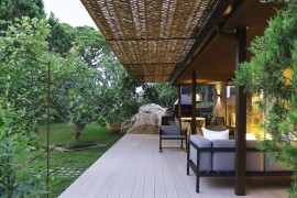 Wooden deck, wicker and iron pergola extend the living area into the lush green garden