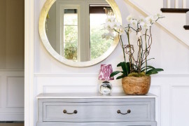 Clean and elegant decor with sparkling round mirror and dresser near stairway