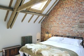 Farmhouse style bedroom with wooden ceiling beams, skylight and exposed brick wall [Design: PAD studio]