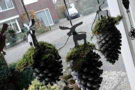 Pinecones with moss and reindeer figurines hung in window
