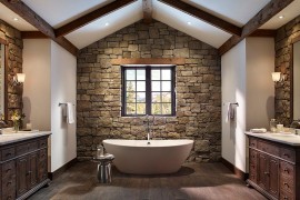 Rough cut stone wall and wooden ceiling beams create a cozy ambiance in the bathroom