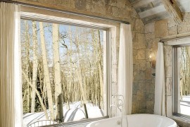 Rustic bathroom with stone wall, vintage bathtub and antler chandelier