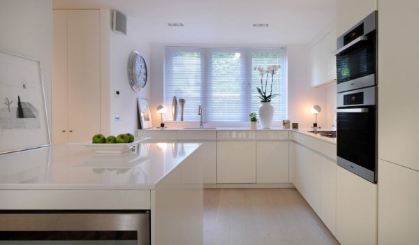 White fruit bowl with green apples placed on a white kitchen island.