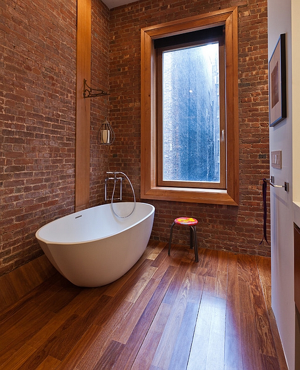 Exposed brick wall and warm wooden floor complement the modern bathtub elegantly