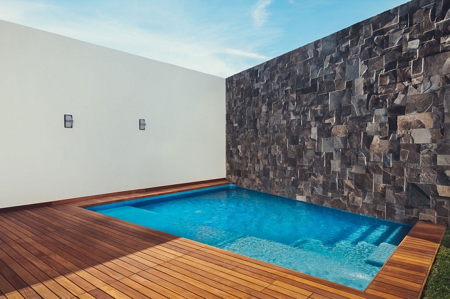 Private pool with a wooden deck and a stone wall on the side