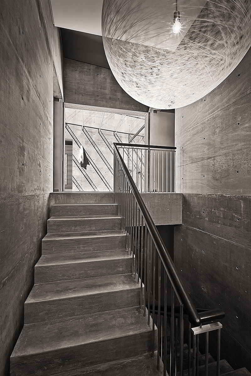 Dramatic pendant light and the concrete backdrop create a monochromatic setting for the staircase