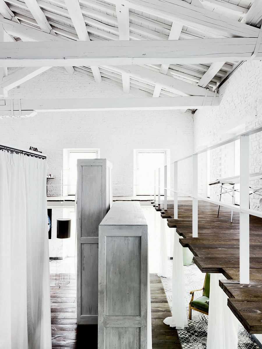 High ceiling with exposed and painted wooden beams and mezzanine level inside the industrial home