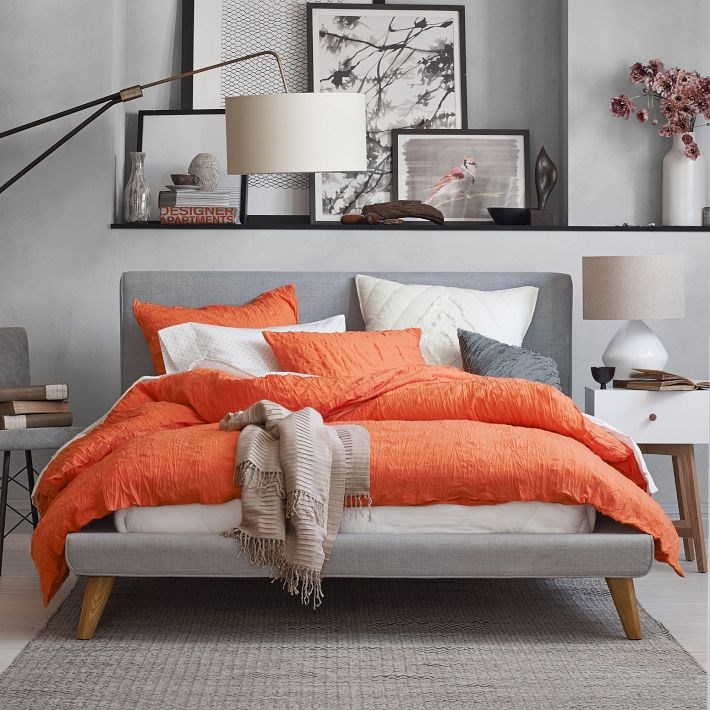 Grey upholstered bed with tangerine bedding