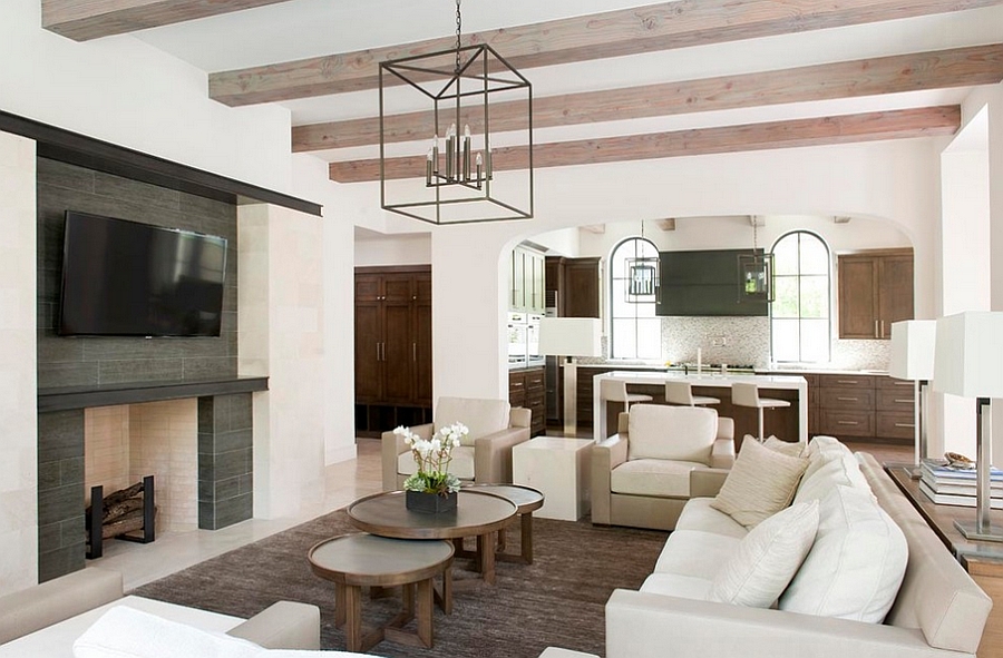 Tanner Round Coffee Table - 1 / An iron and glass lantern lights a round teak coffee table placed on a light gray rug in front of a gray sofa.