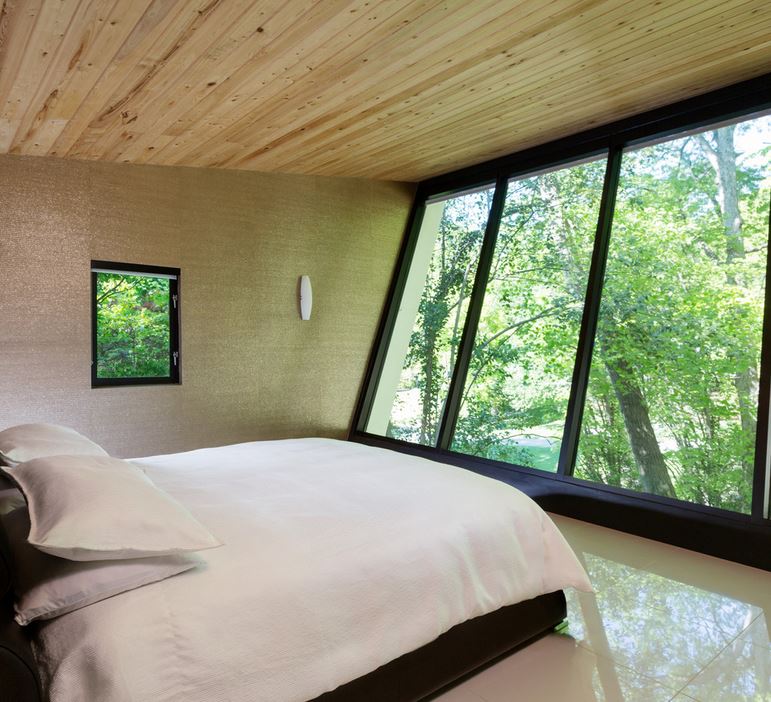 Modern bedroom with slanted windows and a forest view