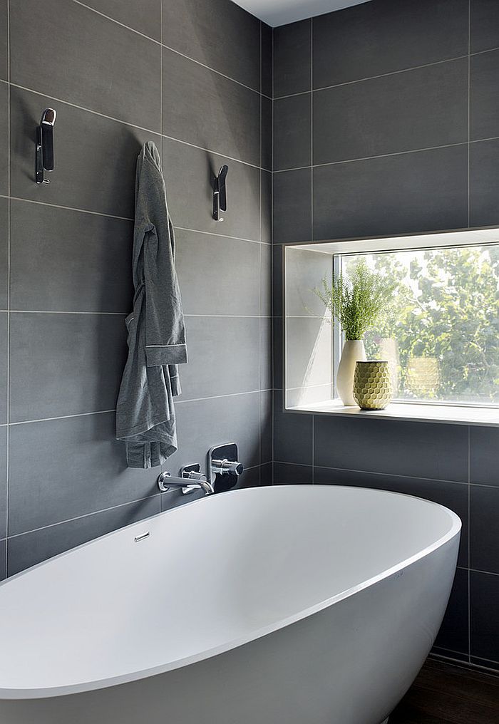 Standalone bathtub in white in a bathroom with gray wall tiles