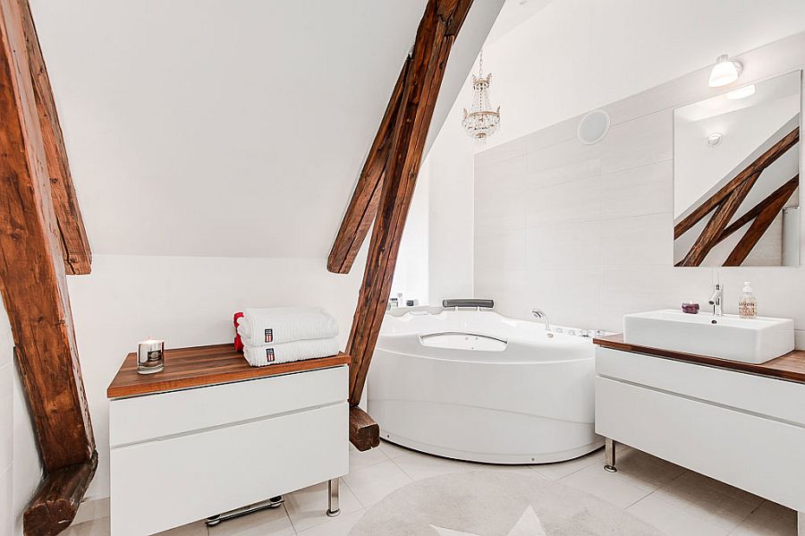 Wooden beams of the attic apartment add a unique visual to the soothing bathroom in white