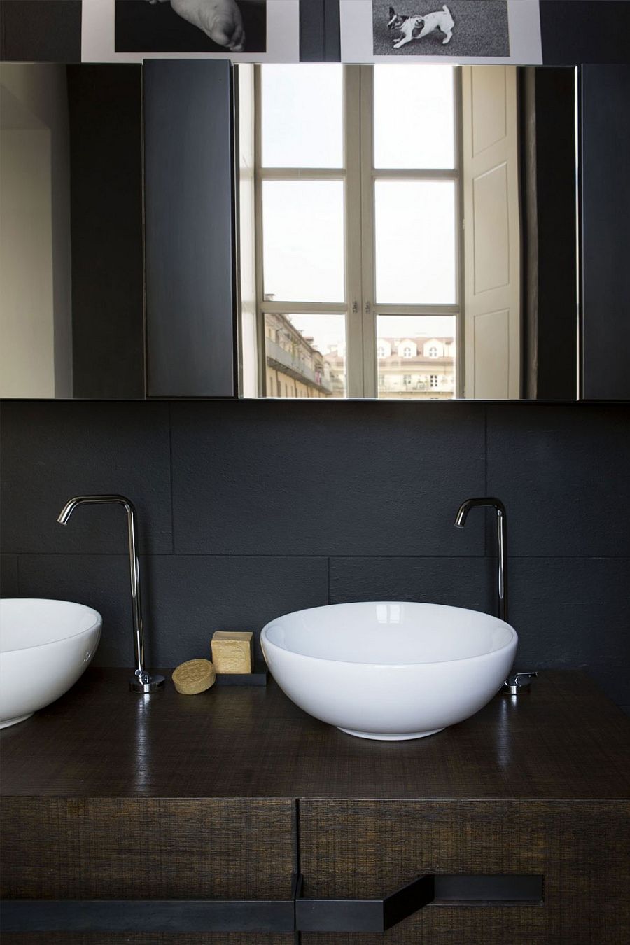 Black backdrop and white sinks along with a wooden vanity in the bathroom