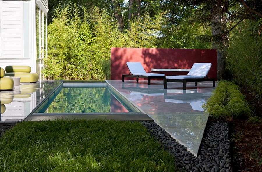 Narrow pool in the backyard of a modern house with lounge seating.