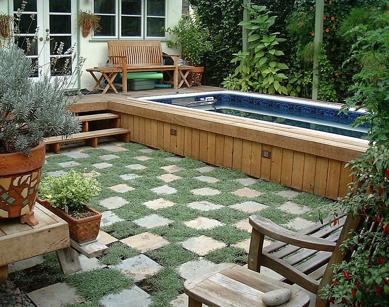 Above-ground small pool with wooden stairs leading to concrete and grass ground pavers.