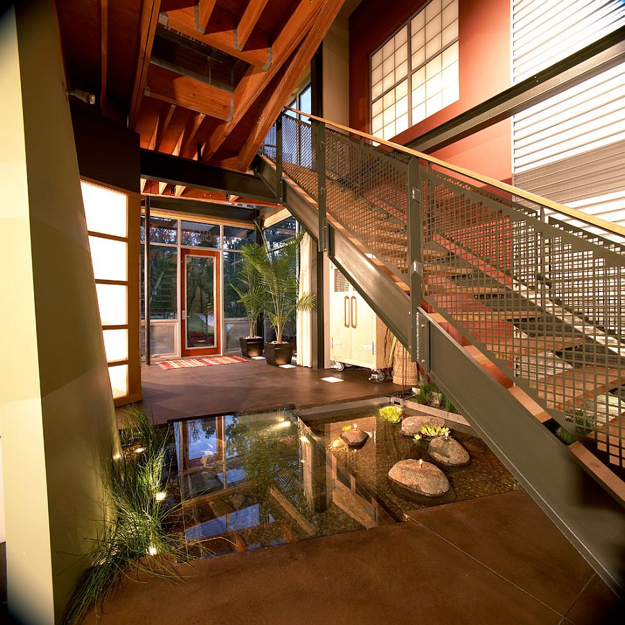 Small indoor water feature with a glass walkway and a staircase above [Design: Kevin Akey -AZD Architects]