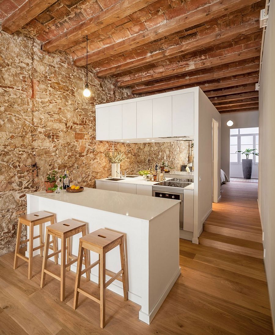 Wooden ceiling beams and stone wall stand in contrast to the sleek white kitchen