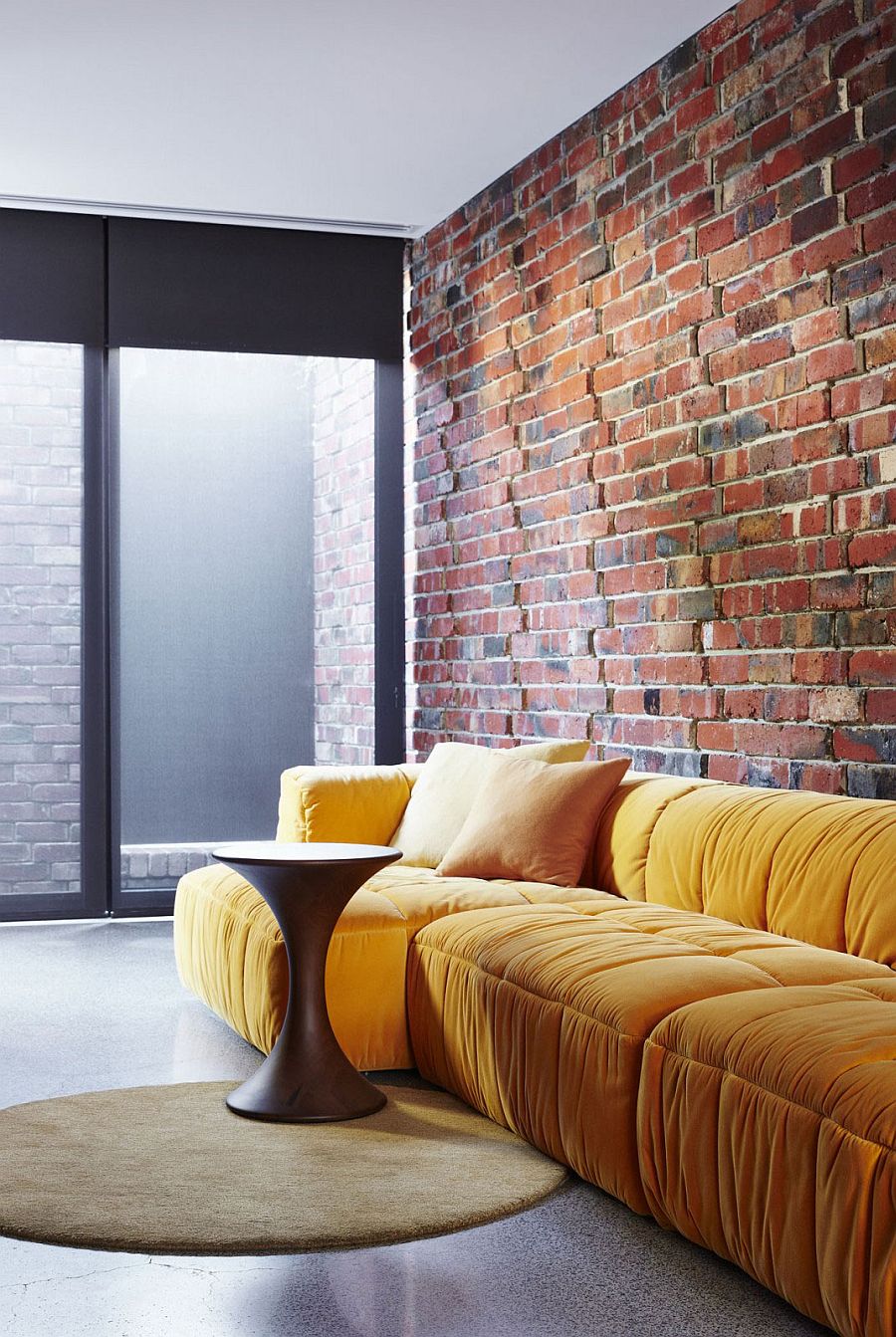 Plush couch in bright yellow adds color to the creative sitting area in brick, glass and steel