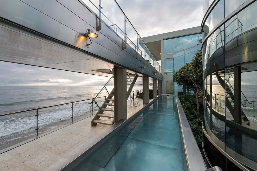 Lap pool and walk way along with an outdoor lounge next to the ocean