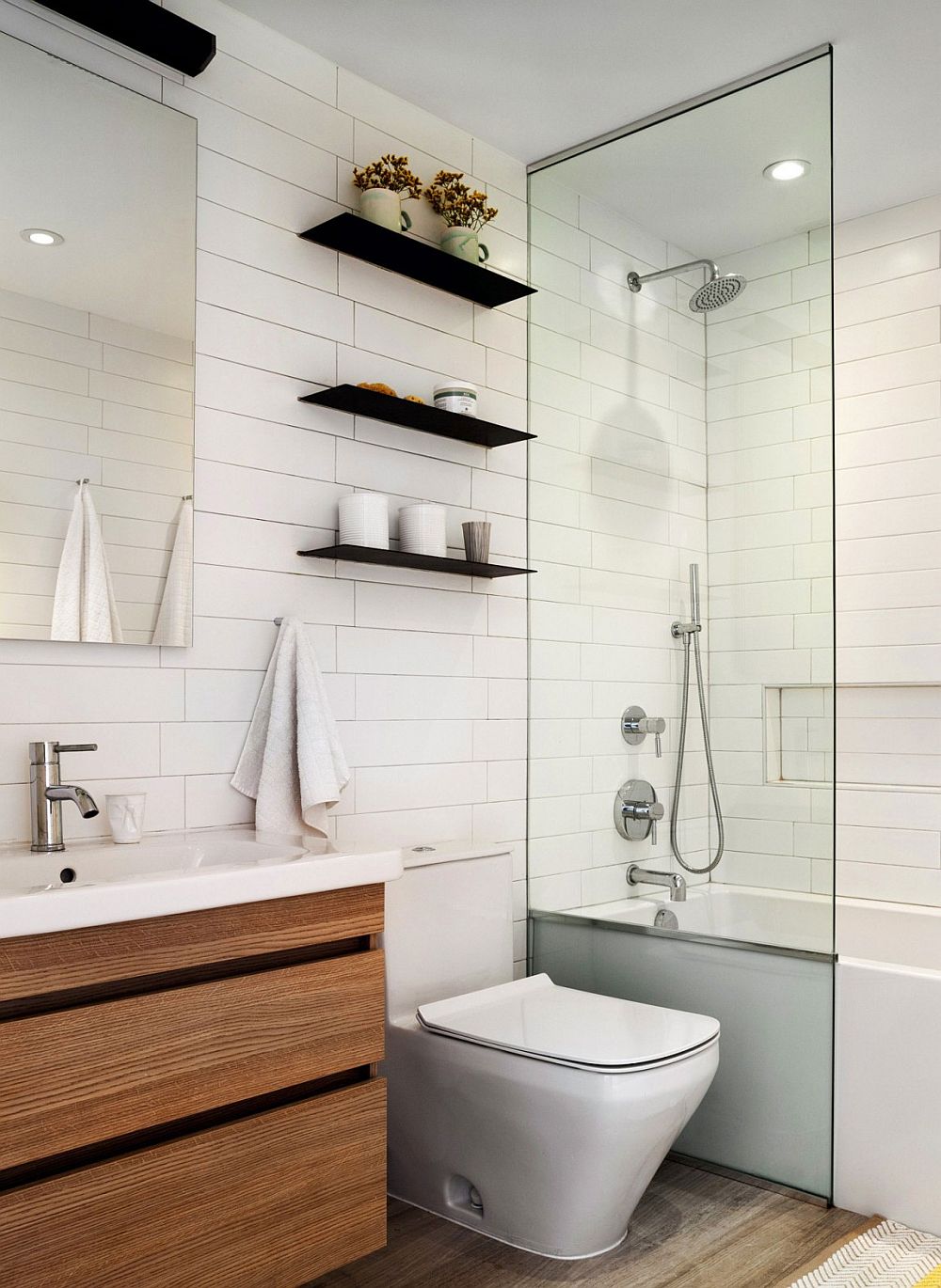 Sleek, dark floating shelves in the all-white contemporary bathroom hold their own