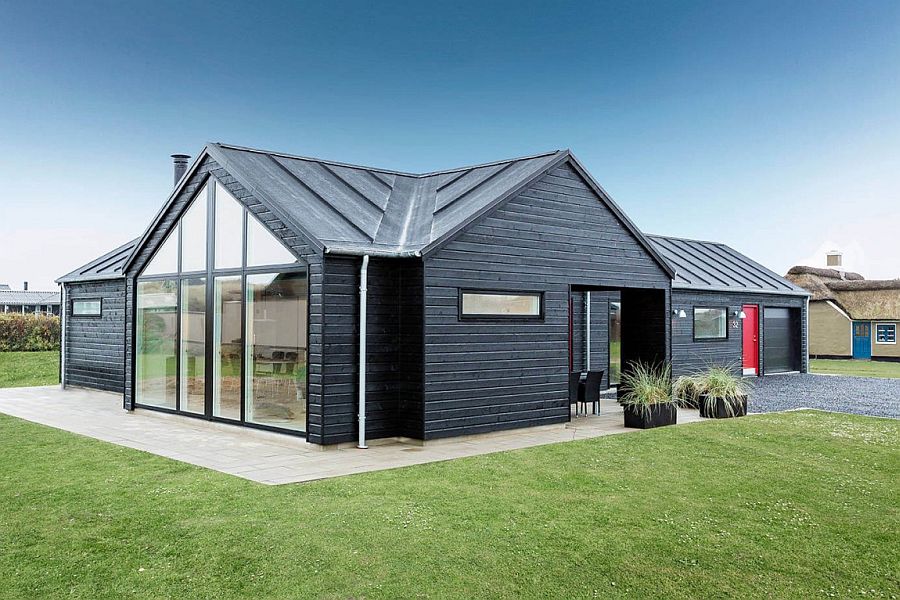 Contemporary black exterior of the summer home with a bright red door