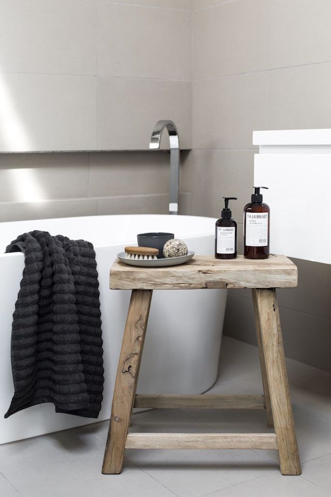 Small rustic zen style stool used for accessories in white bathroom