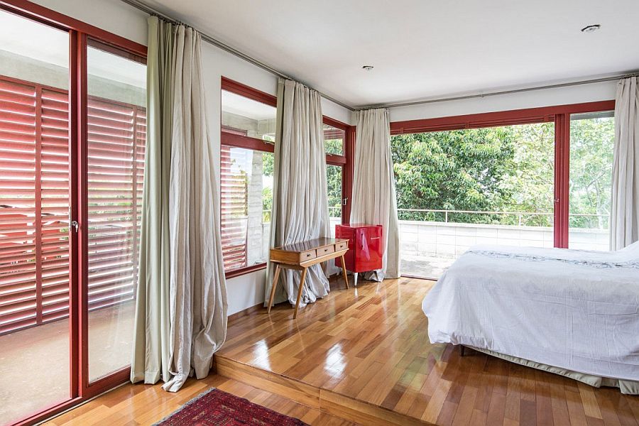 Modern bedroom with white drapes, glass doors with red metallic frames and polished wooden flooring