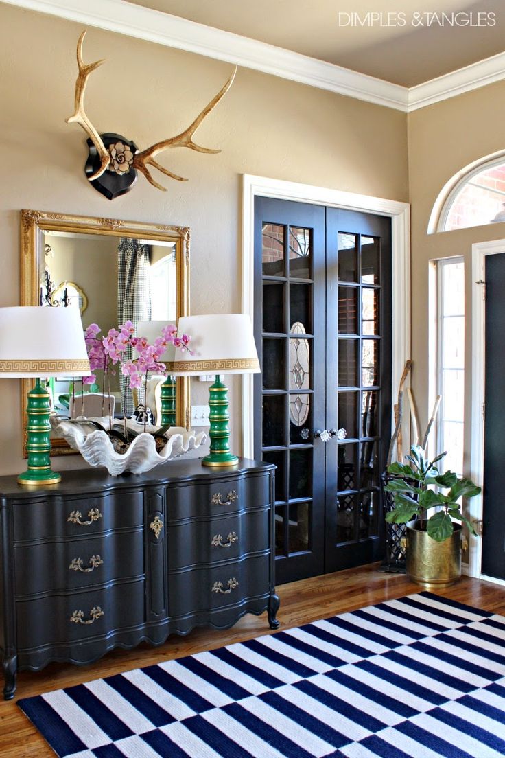 Bold and eclectic entryway with a gold framed mirror and antler decor above it