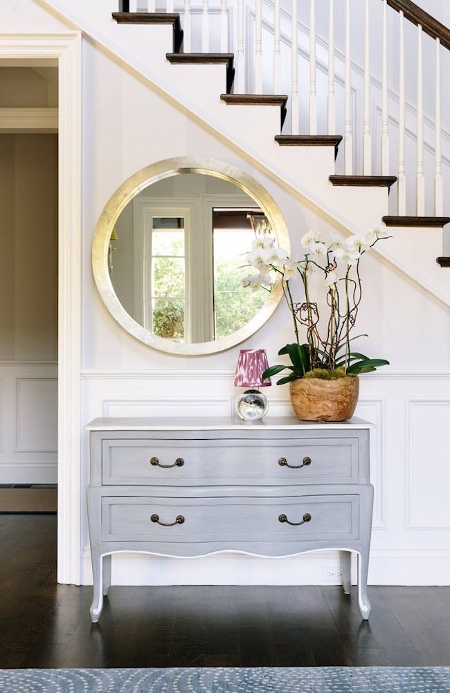Clean and elegant decor with sparkling round mirror and dresser near stairway