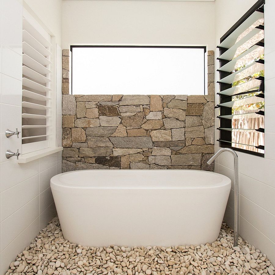 Half wall in natural stone and pebbles on the floor turn the the small bathroom into a relaxing hub