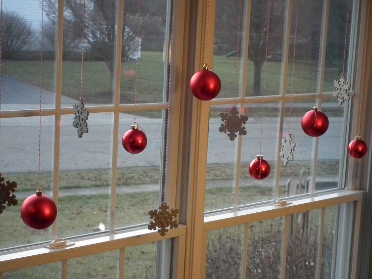 Red glass balls and snowflake ornaments hung in window.