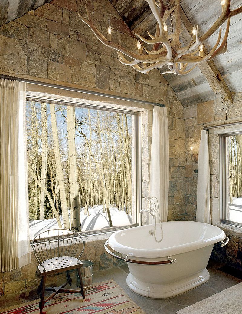 Rustic bathroom with stone wall, vintage bathtub and antler chandelier [Design: JLF & Associates]