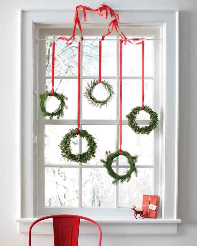 Tiny wreaths hung with red ribbon in a window