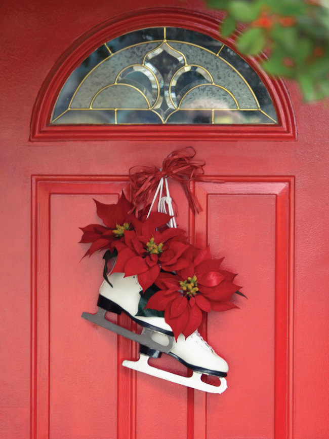 A pair of skates with some festive poinsettias hangs on a red door