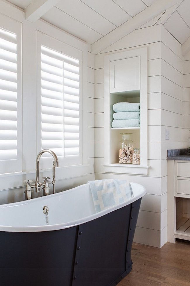 Bathroom with shiplap walls and built-in storage shelving near freestanding bathtub