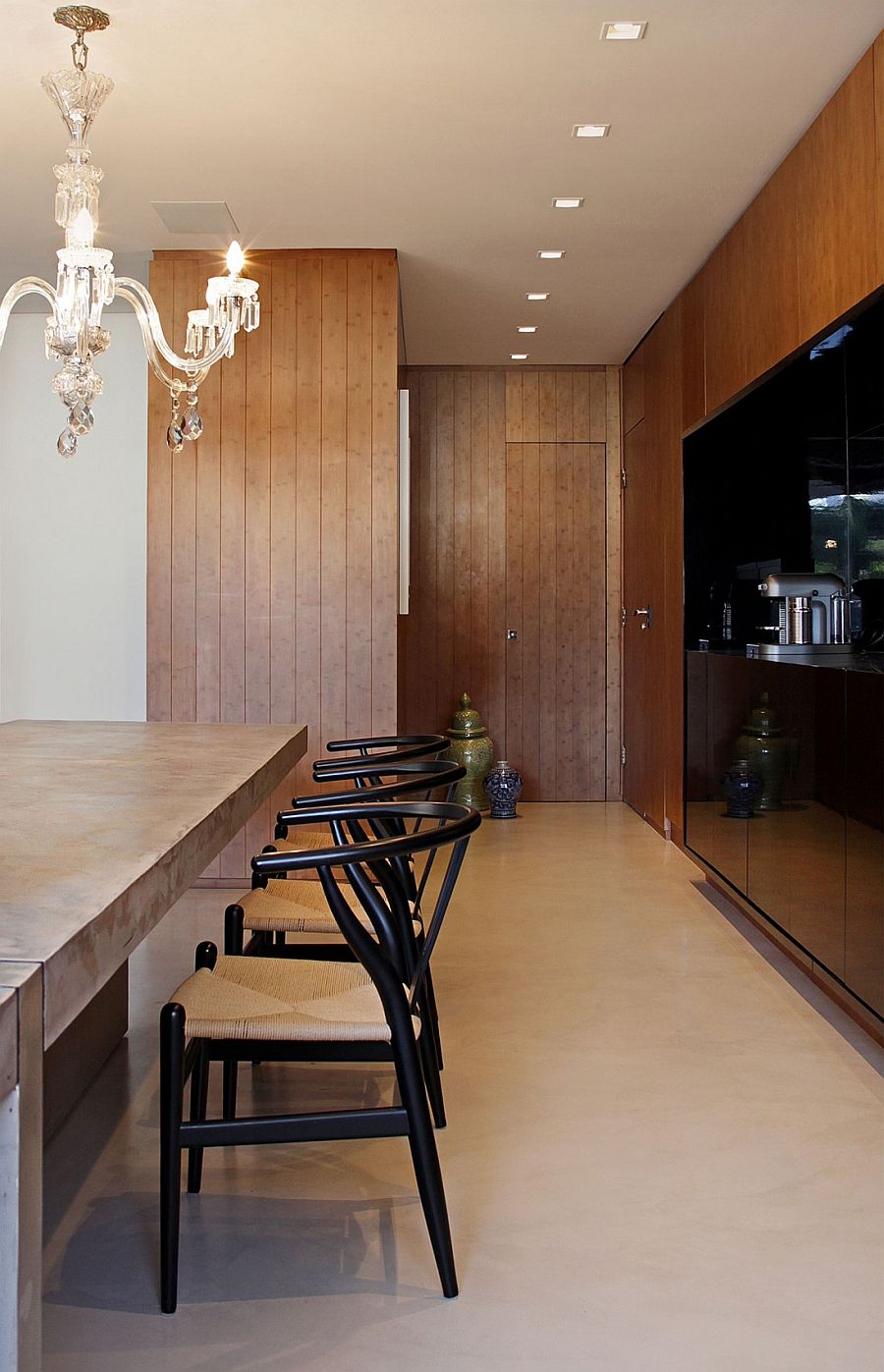 Dark wall in the kitchen, beautiful chandelier and wishbone chairs inside the Brazilian apartment