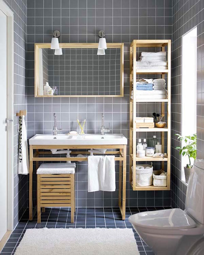 Gray tiled bathroom with wood furniture and shelving unit attached to wall