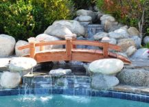 Arched-wooden-bridge-over-the-water-garden-is-a-great-way-to-complete-your-poolscape-217x155