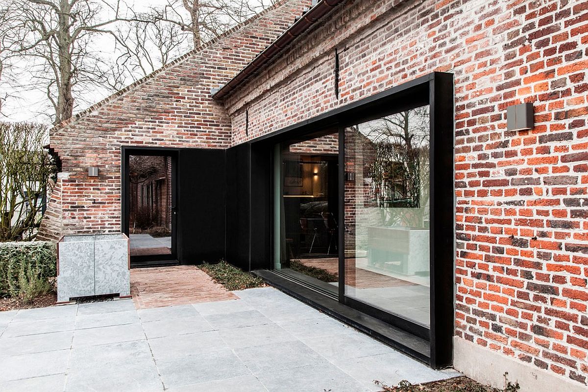 Brick exterior of the old farm house given a new, dark window with sliding glass doors