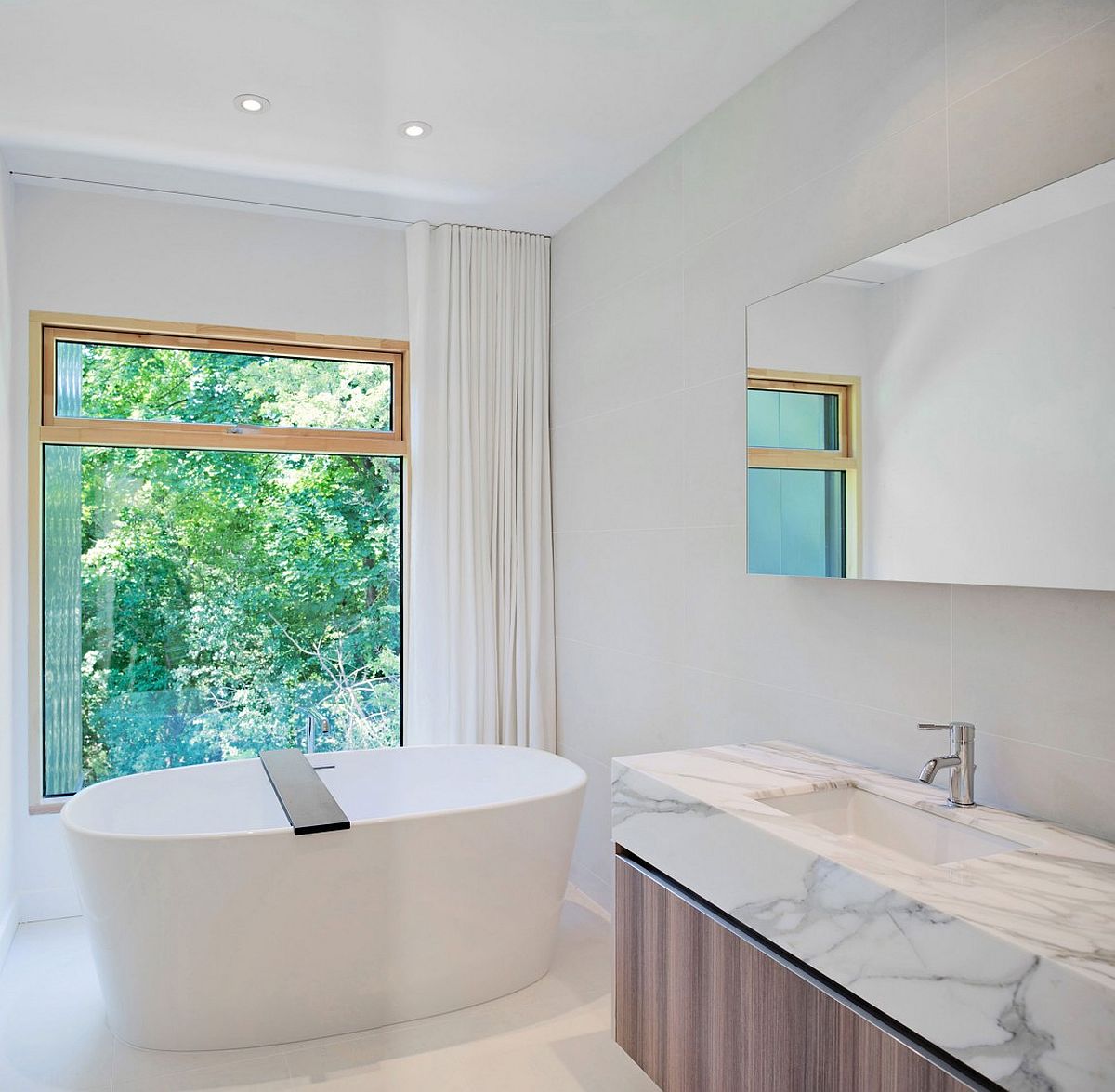 Standalone bathtub and vanity with wooden base and marble top inside the contemporary bathroom