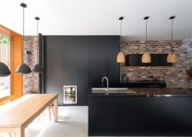 Dark-kitchen-cabinets-and-contemporary-island-sit-next-to-the-exposed-brick-wall-217x155