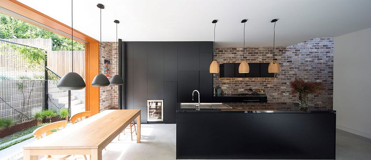 Dark kitchen cabinets and contemporary island sit next to the exposed brick wall