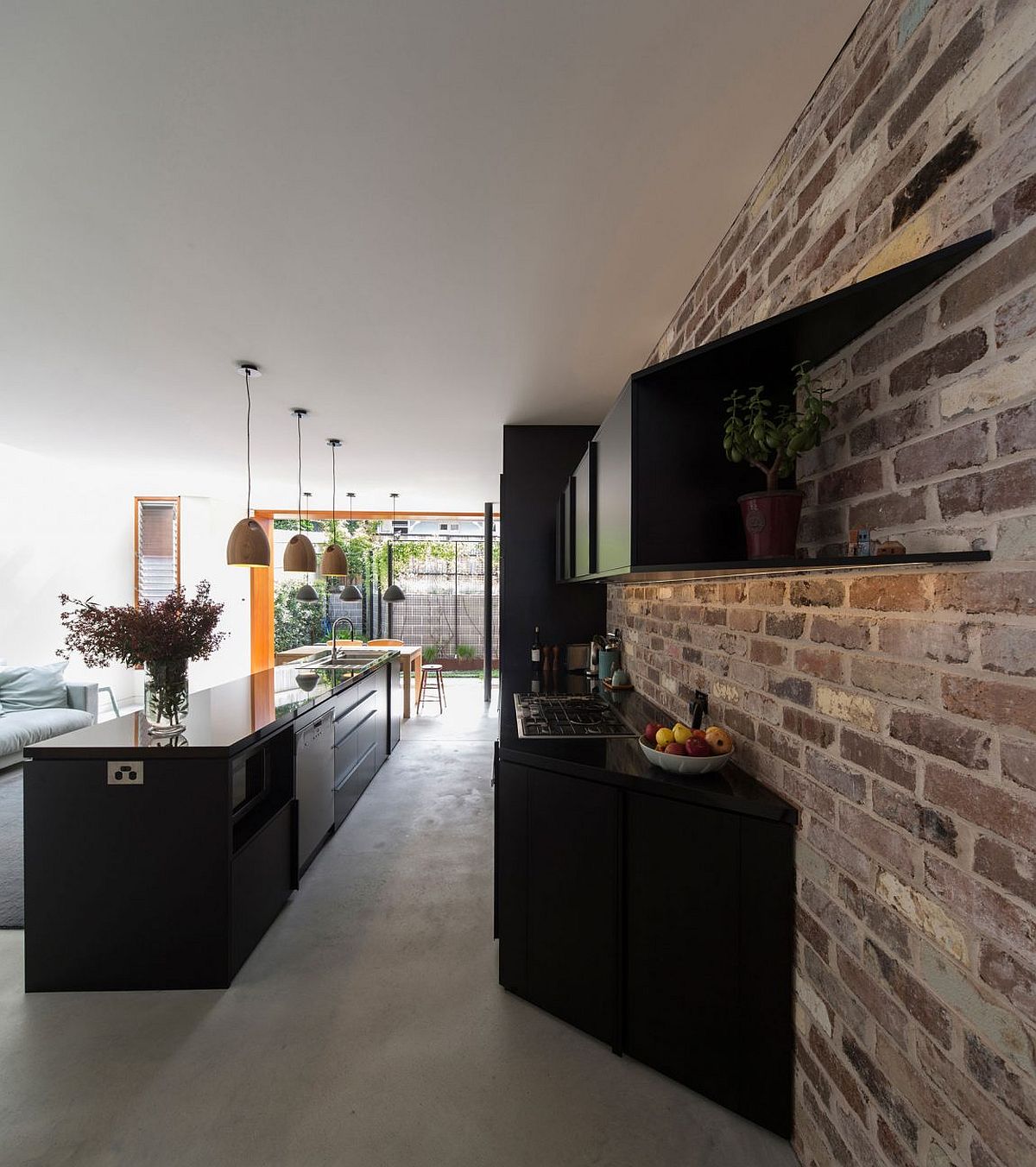 Glossy black kitchen cabinets coupled with exposed brick wall to create textural beauty