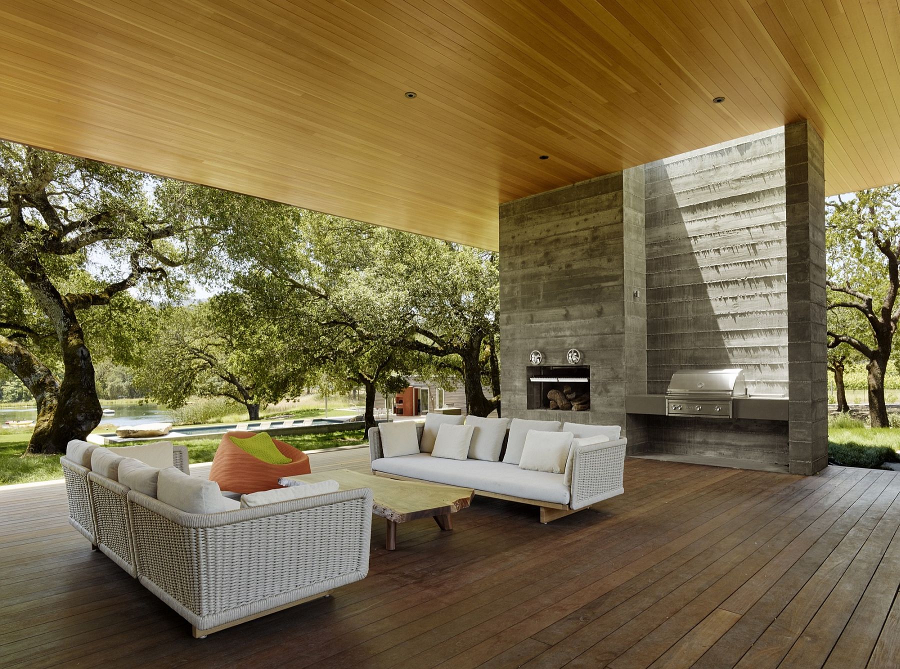 Open, outdoor living areas with shade overlook the natural pond and the greenery beyond