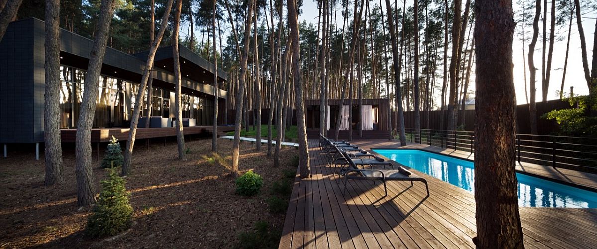 Pool area and deck next to the modern chalet surrounded by tall pine trees