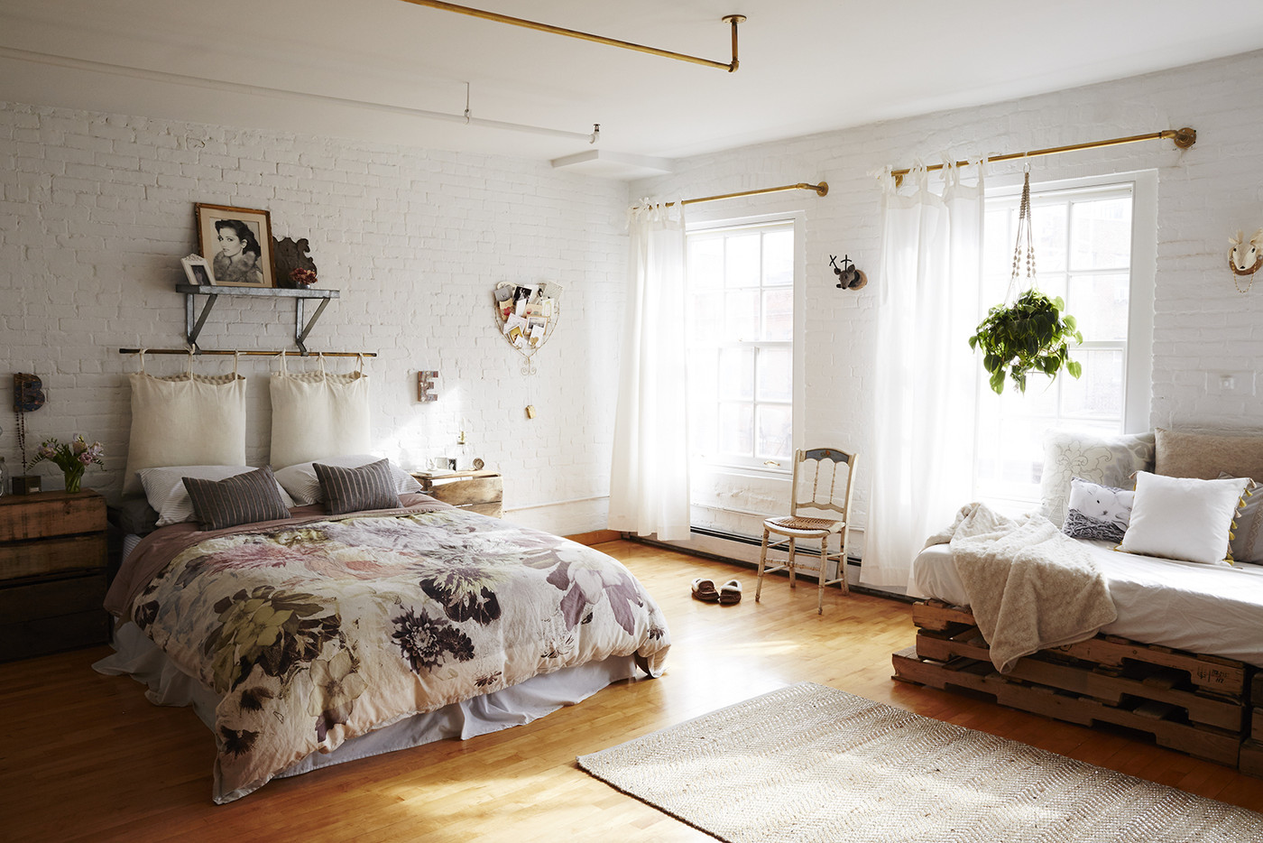Studio apartment with bed, exposed white brick walls, and a couch made of wooden pallets.
